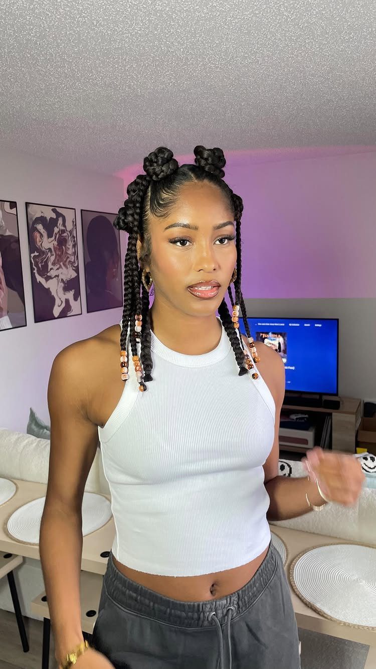 A young woman showcasing her hair styled in small Bantu knots and long braids.