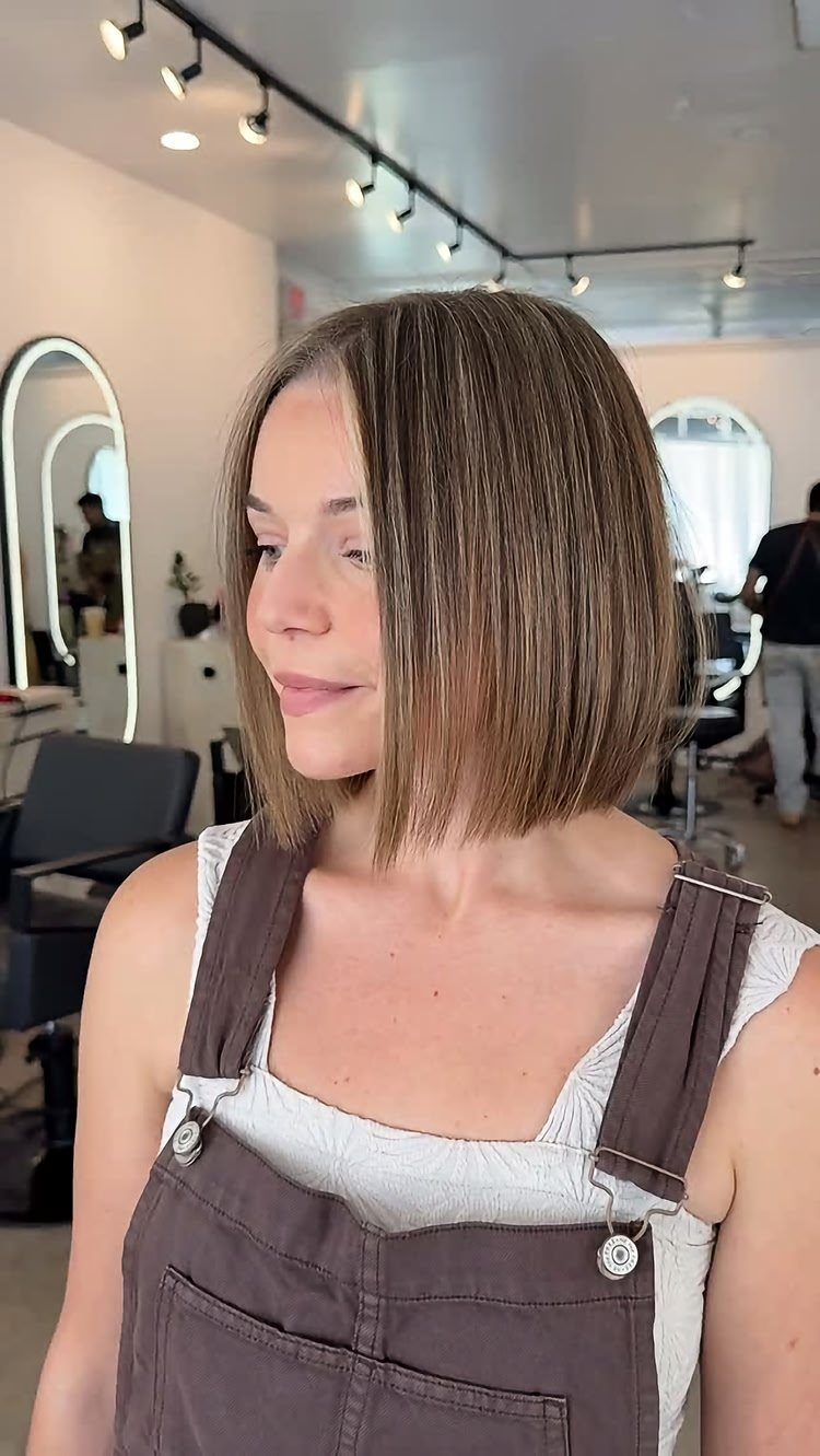 A woman showcasing a straight, chin-length blunt bob hairstyle in a hair salon.