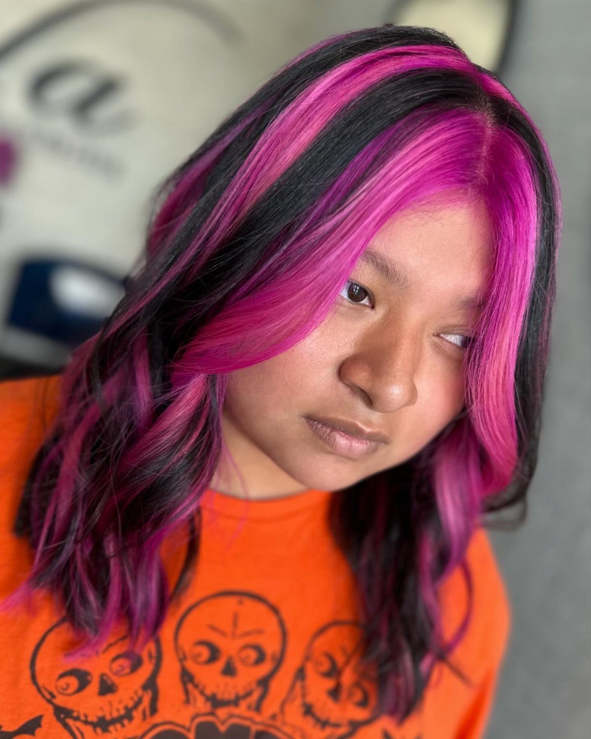 A person with long dark hair featuring bold, thick pink chunky highlights and wavy texture.