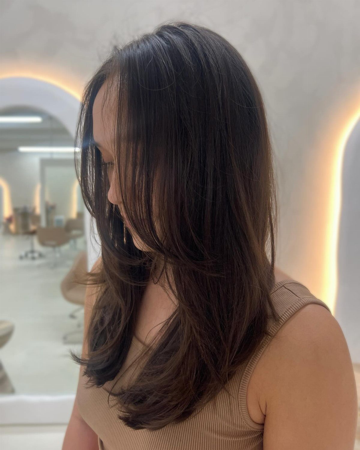 Woman with long dark brown hair featuring layered face-framing cuts in a salon setting.