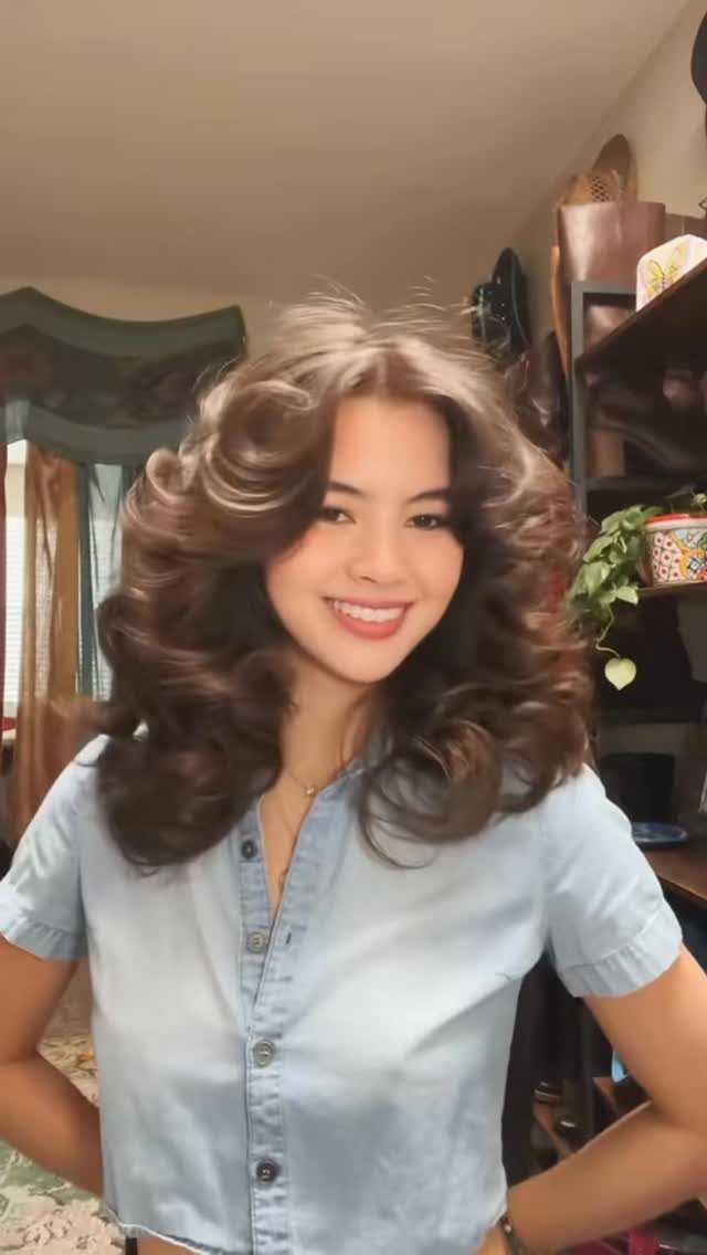 A smiling woman with voluminous brown hair and soft, layered feathered bangs.