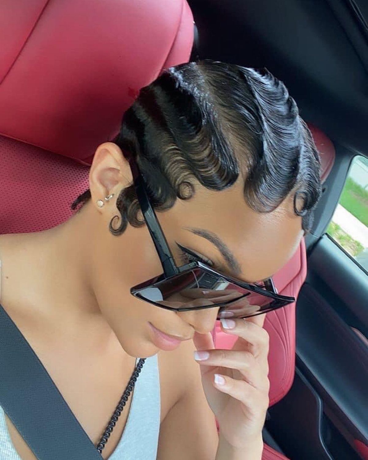 A woman with dark hair styled in glossy, sculpted finger waves wearing black sunglasses.