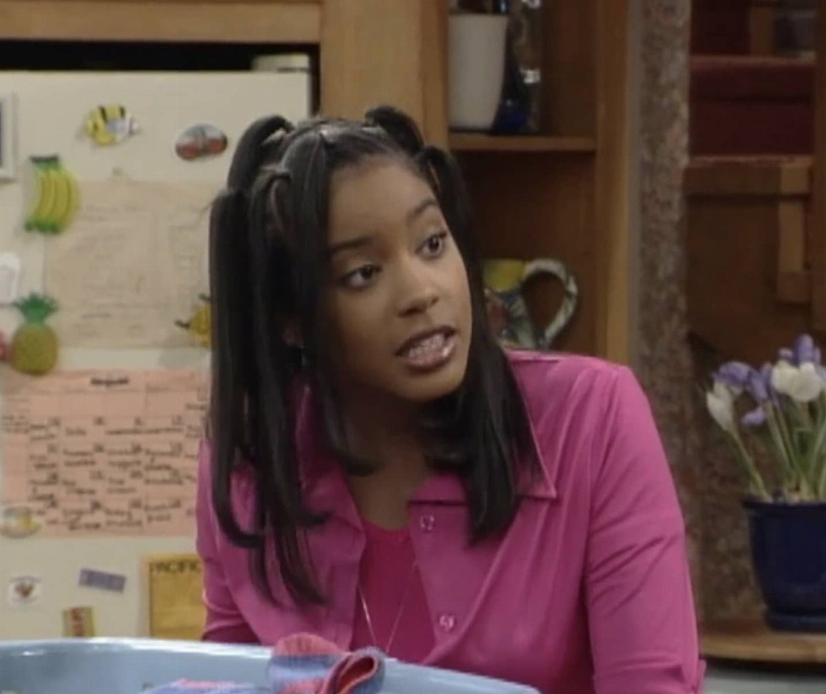 A young woman with dark hair styled in 90s-style half-up pigtails wearing a pink shirt.