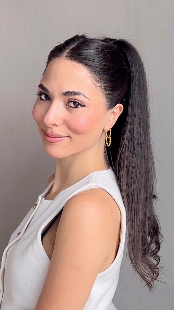 A woman with dark hair styled in a sleek, high ponytail against a grey background.