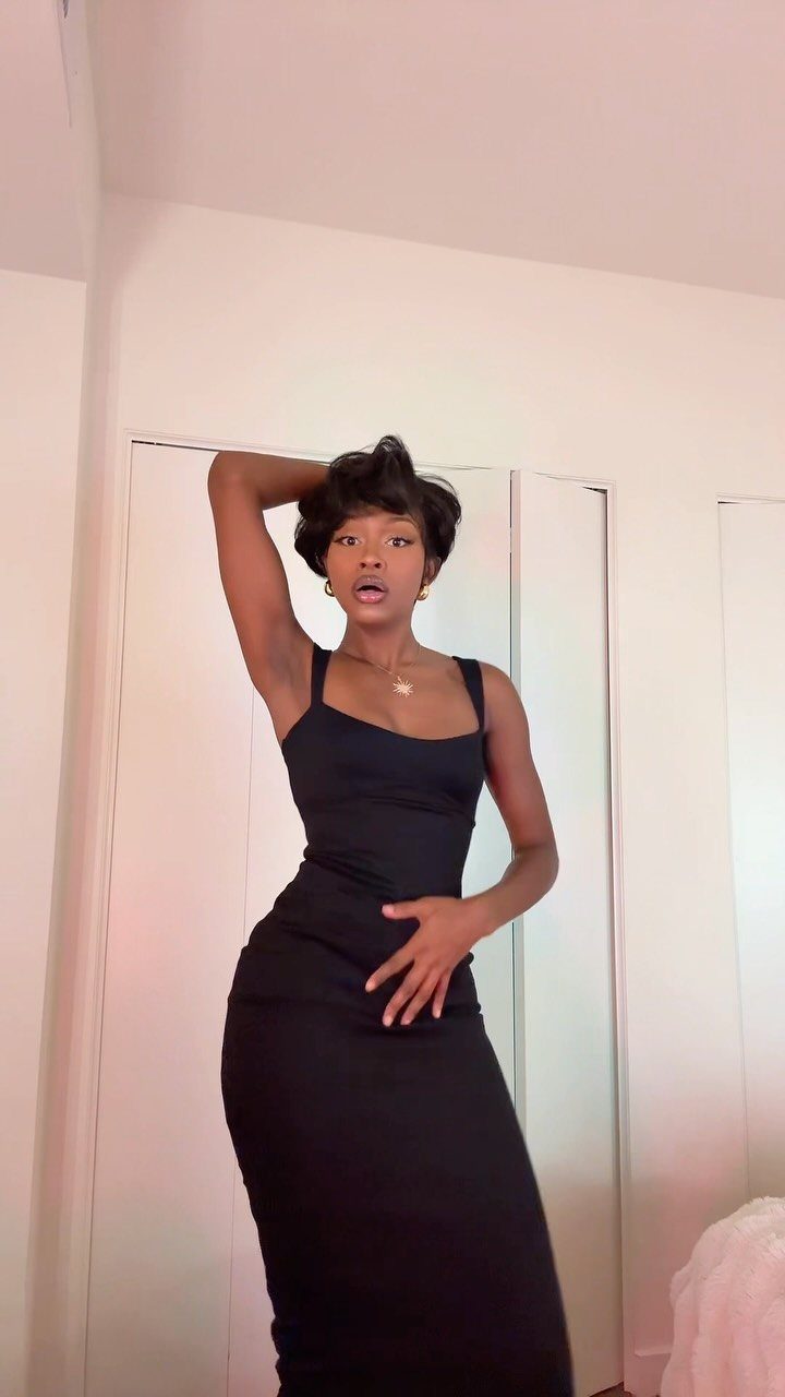 A woman with a short dark pixie cut posing in a black dress.