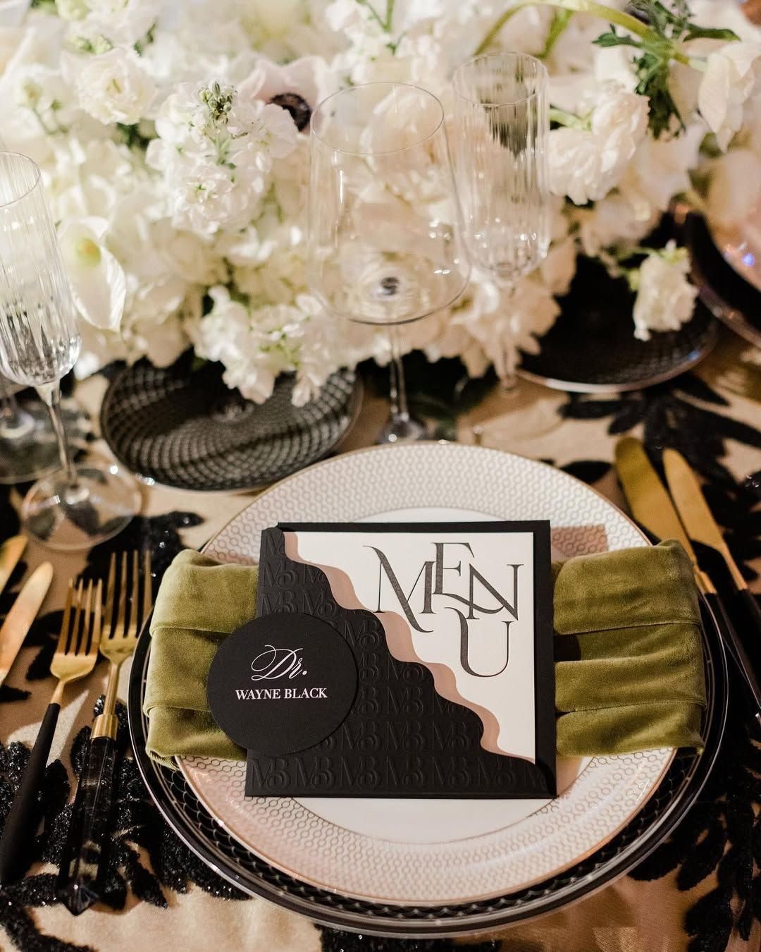 A white textured plate sits on a black beaded charger plate with a menu and gold cutlery.