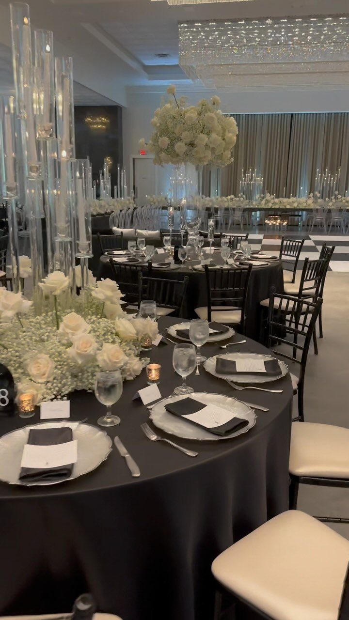 A wedding table set with a black tablecloth, white floral centerpieces, and black napkins.
