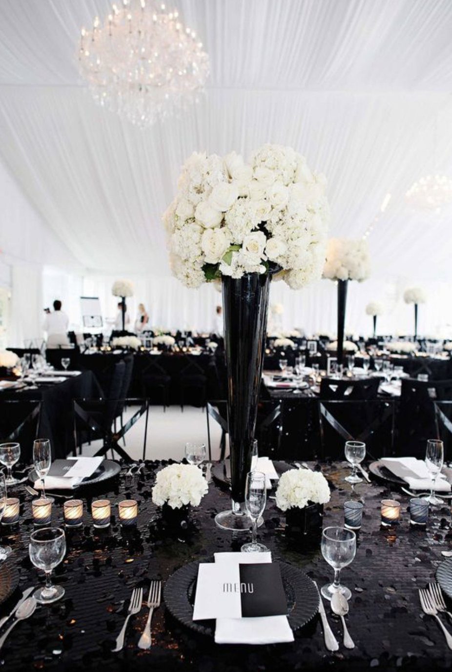 Tall black vase with large white floral arrangement on a black sequined wedding table.