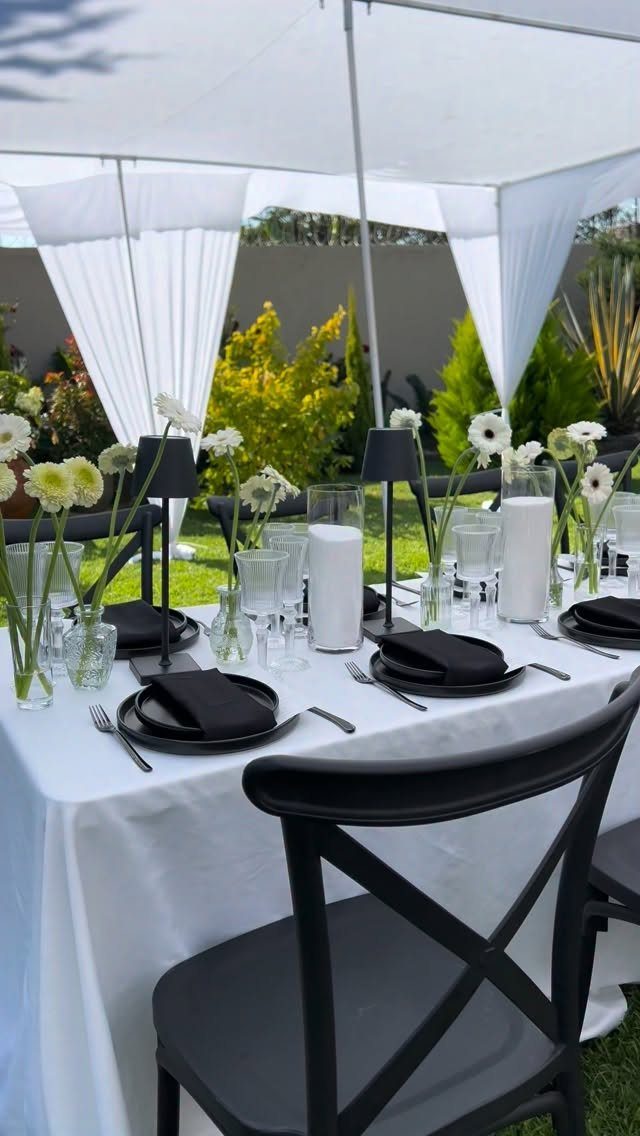 A white wedding table set with black plates, black napkins, and small white flowers in glass vases.