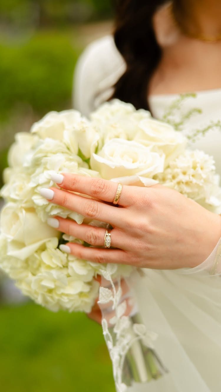 A bride holding a white rose bouquet while wearing a wedding ring and lace dress.