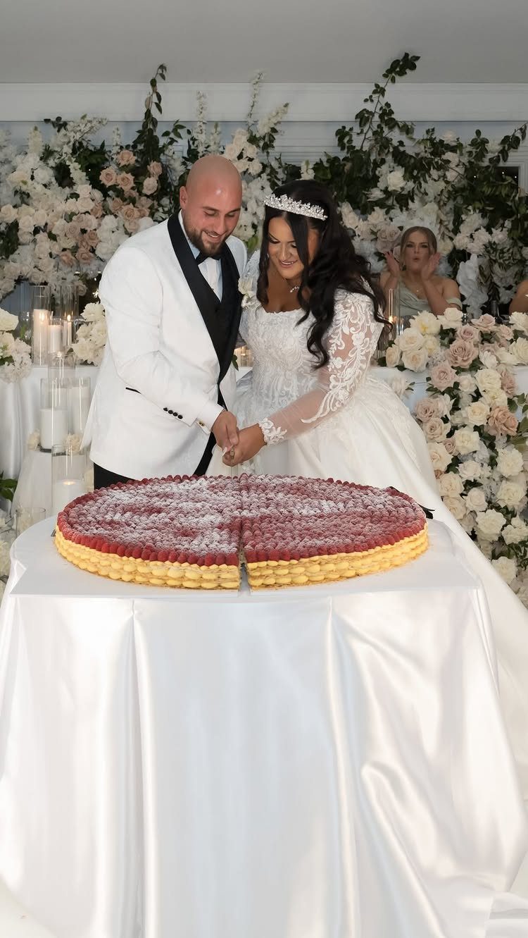 A bride and groom cutting a large round red and white cake at their wedding.