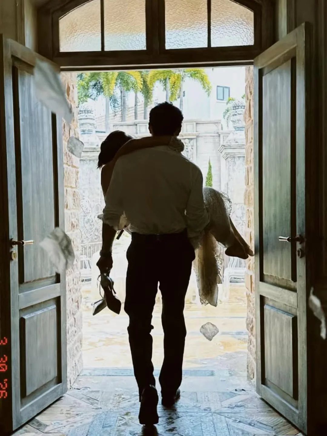 A groom carrying his bride through an open doorway amidst flying white petals.