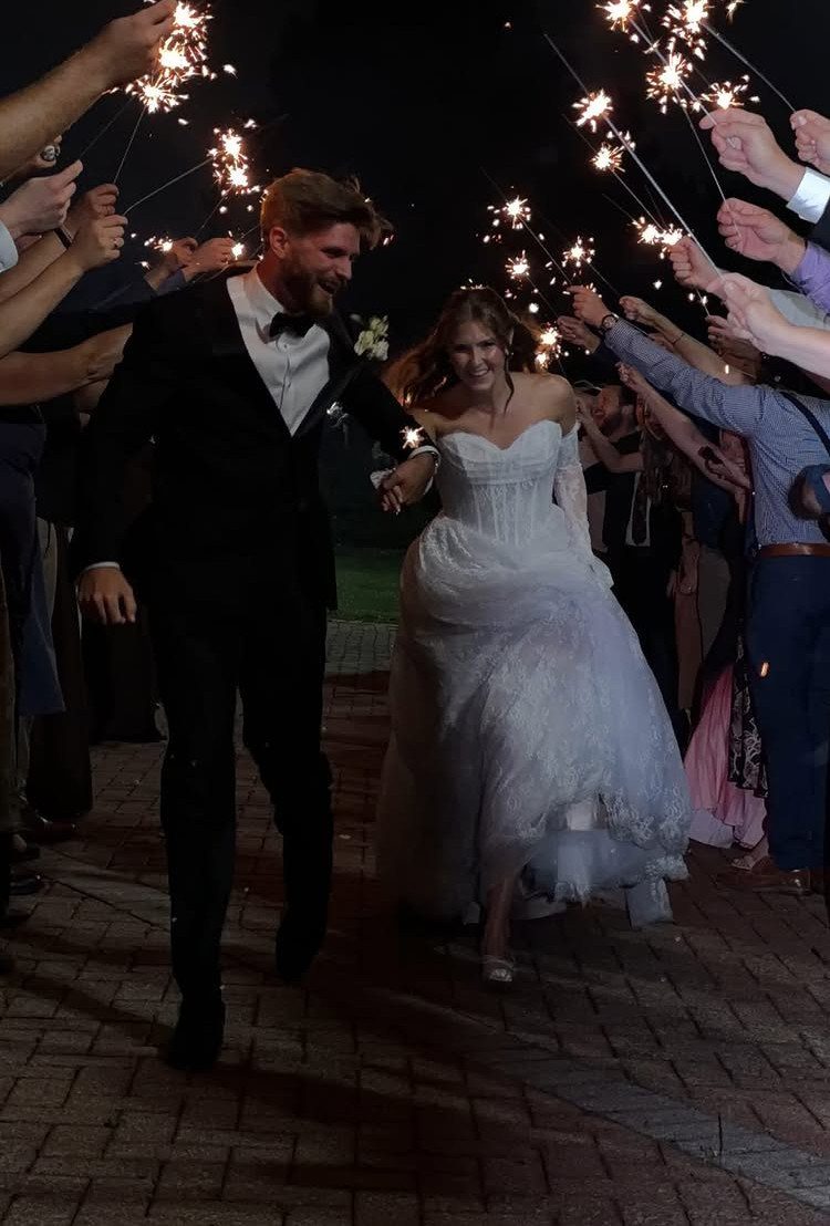 Bride and groom walking through a sparkler send-off tunnel held by wedding guests at night.