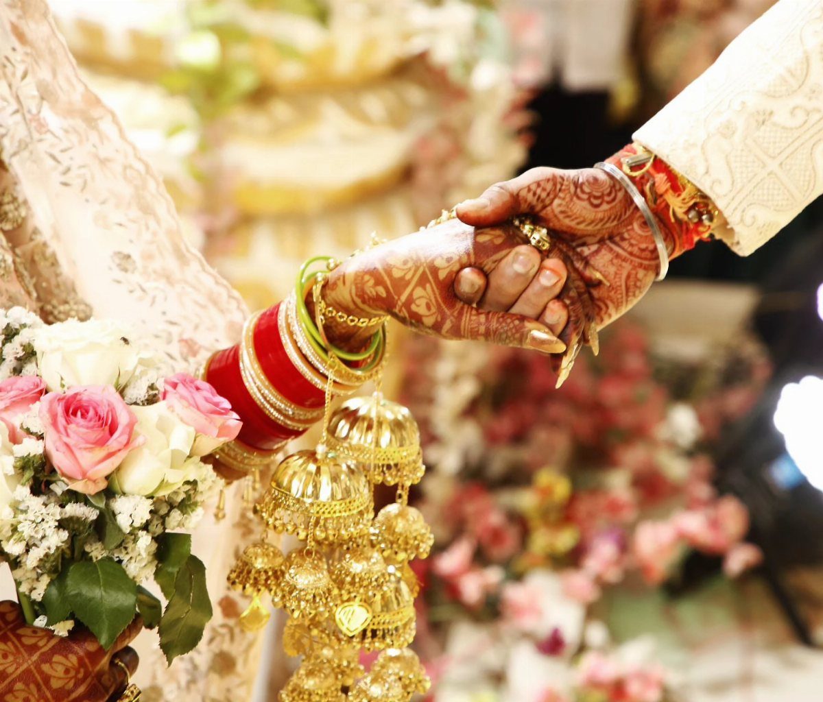 Bride and groom holding hands with henna designs and gold jewelry visible.