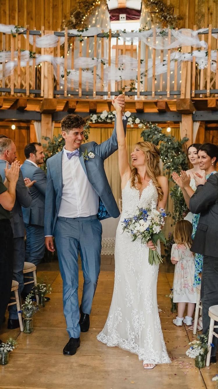 Bride and groom joyfully walking down the aisle while holding hands raised high.
