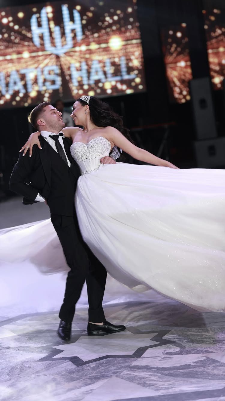 Groom lifting a smiling bride in a white gown on a dance floor.