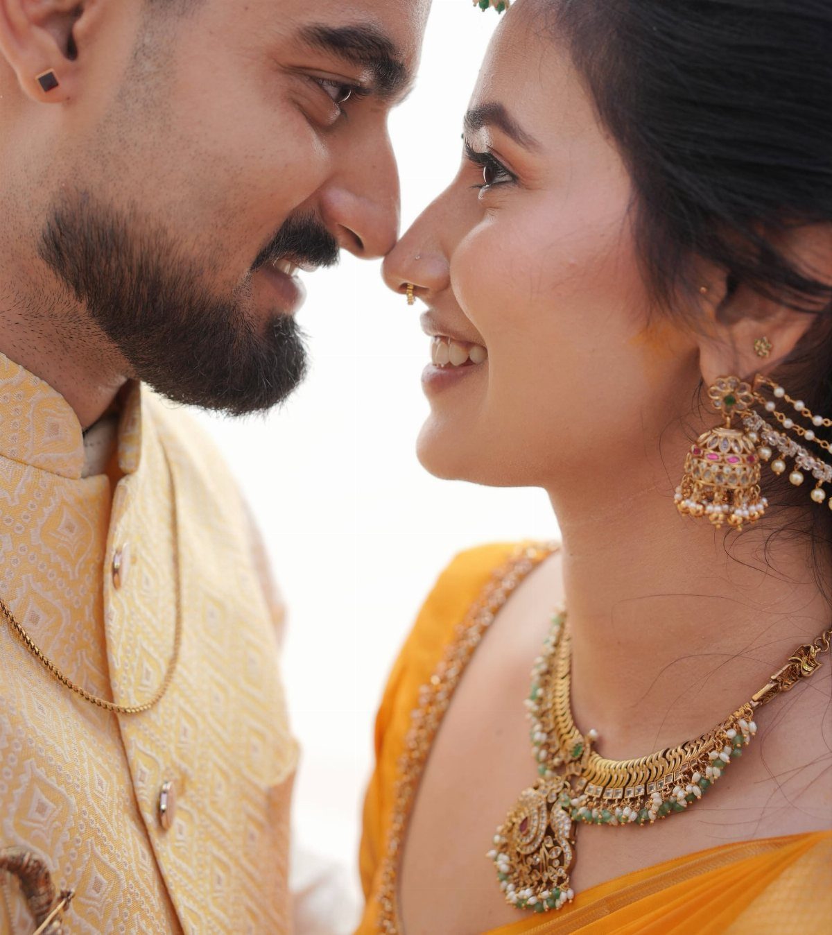A smiling Indian bride and groom in traditional wedding attire facing each other closely.