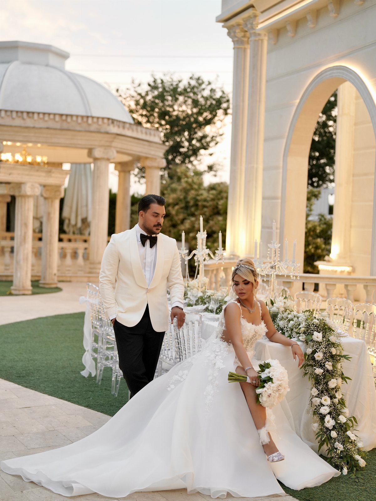 Bride and groom posing by an elegantly decorated outdoor wedding reception table.