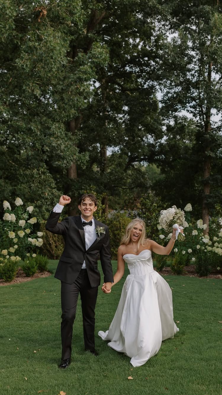 Bride and groom holding hands and walking joyfully through a lush green garden setting.