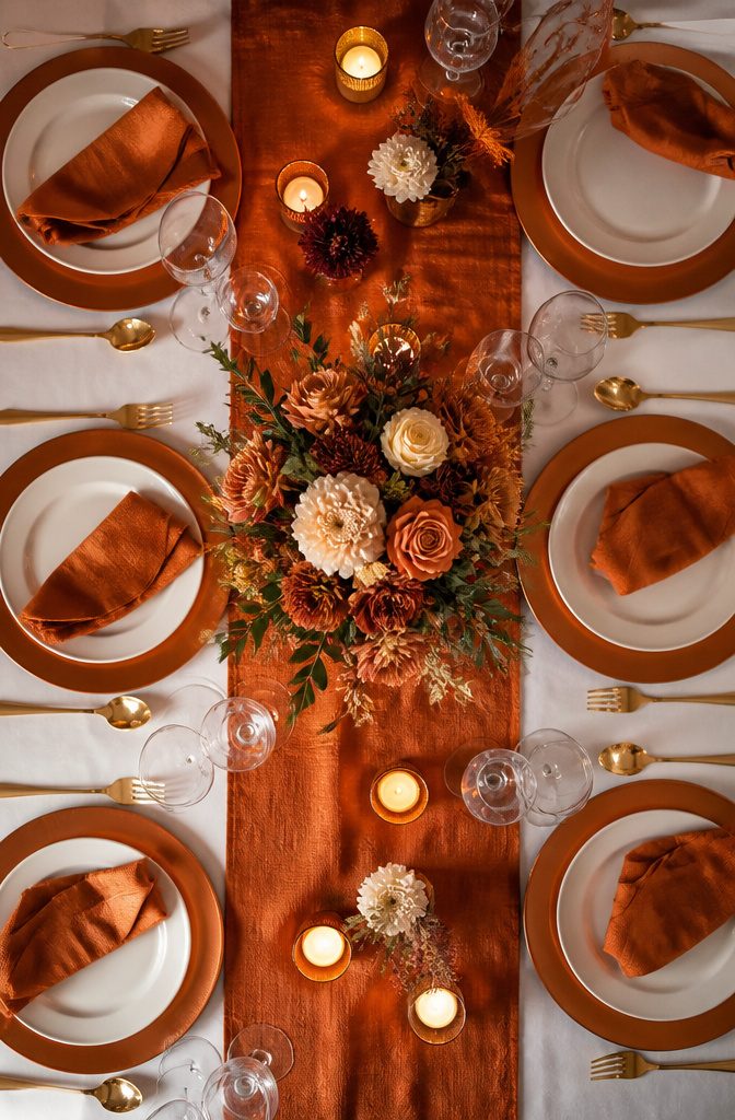 20 Burnt Orange Wedding Decor Ideas for 2026 9 A table setting with a burnt orange runner over a white tablecloth.