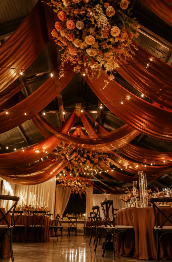 20 Burnt Orange Wedding Decor Ideas for 2026 13 Burnt orange fabric and floral decorations hanging from the ceiling.