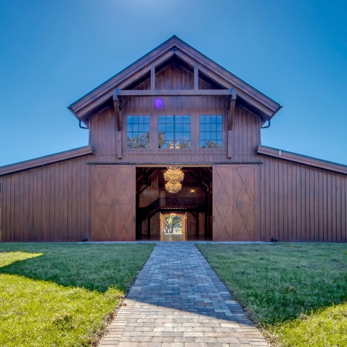 A large brown wooden barn with an open entrance and a stone walkway leading towards it.