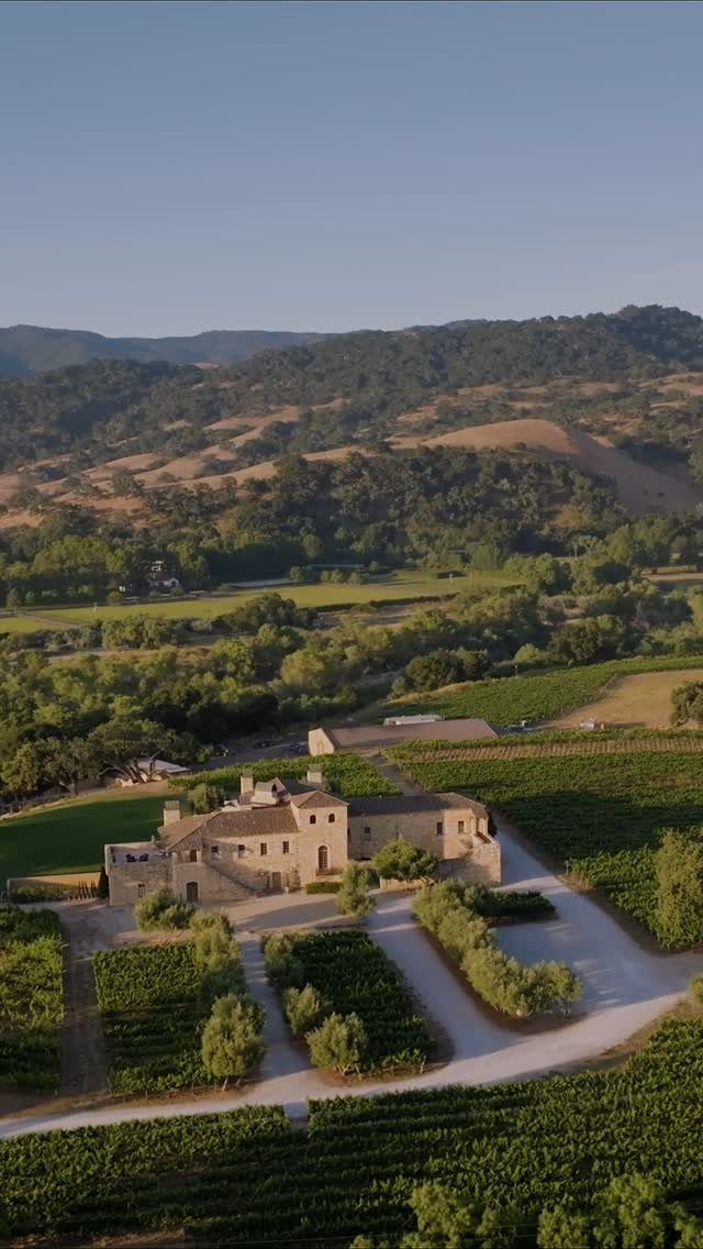 An aerial view of a stone estate nestled among green vineyards and rolling hills.