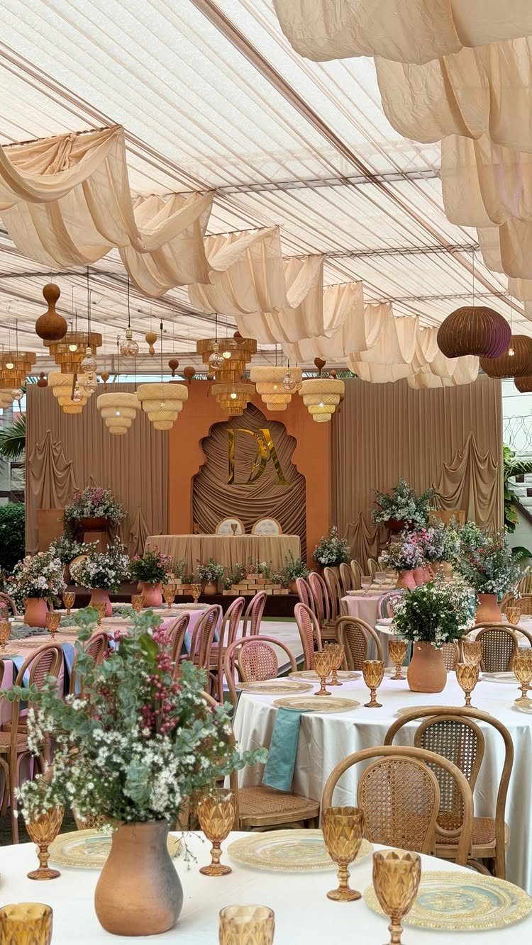 Wedding reception tables decorated with terracotta vases, cream linens, and peach floral arrangements under draped fabric.