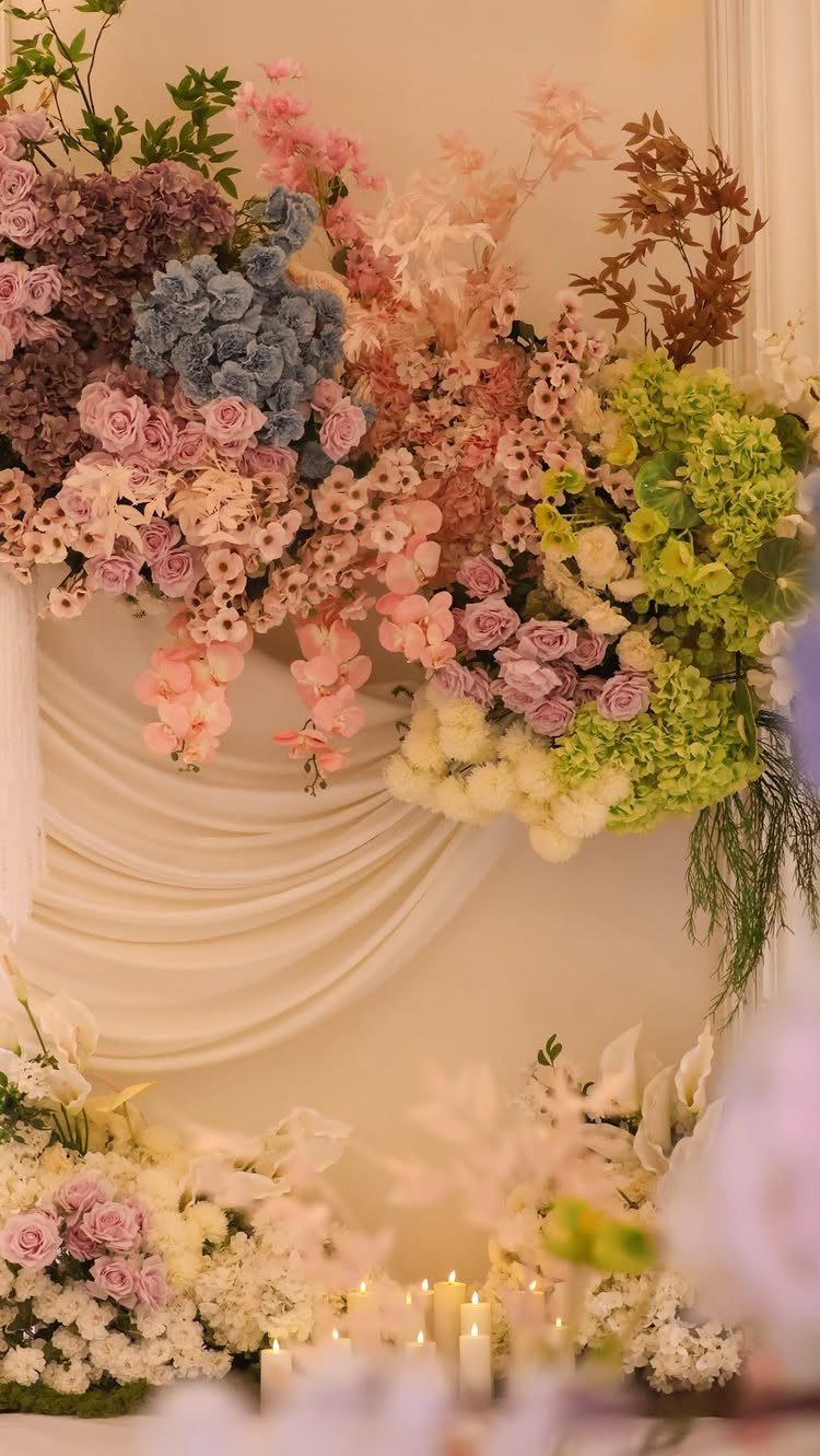 Pastel colored flowers in shades of pink, blue, and green arranged against white draped fabric.
