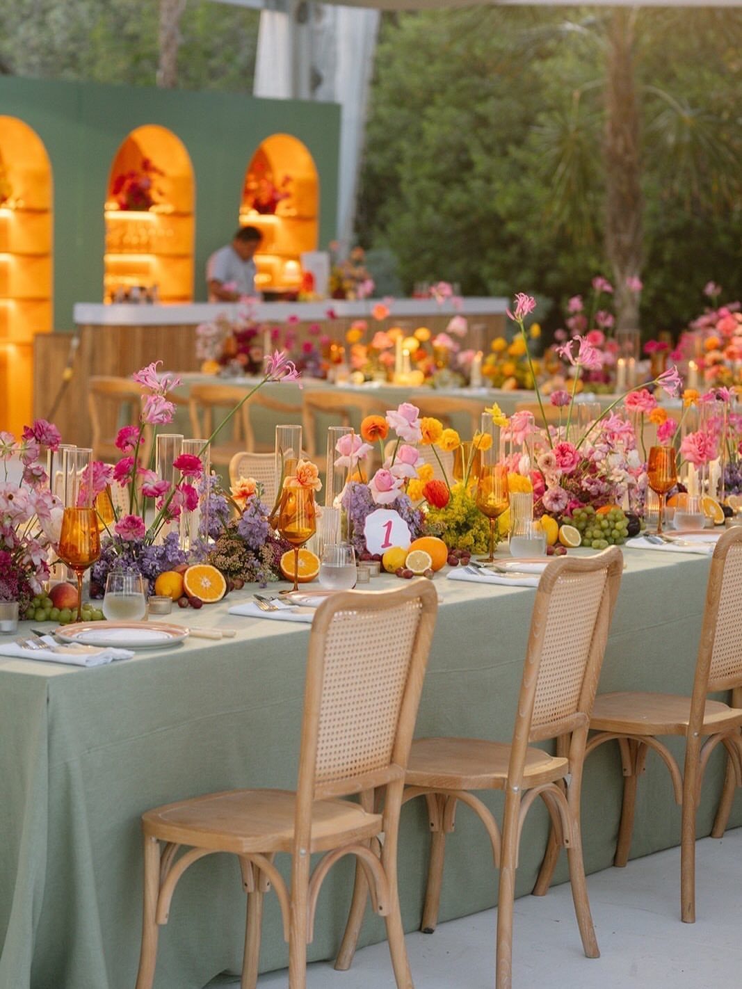 Vibrant pink, coral, and orange floral arrangements decorating a long outdoor wedding reception table.