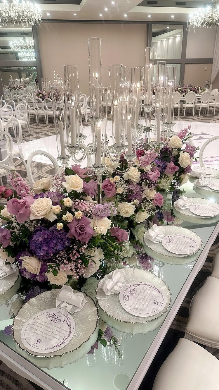 Purple and white floral centerpieces on a formal wedding banquet table with tall glass candle holders.