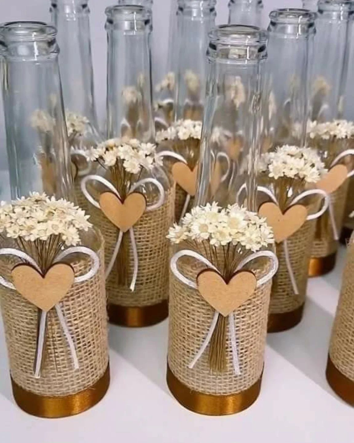 Glass bottles wrapped in burlap with white bows, small hearts, and tiny dried flowers.
