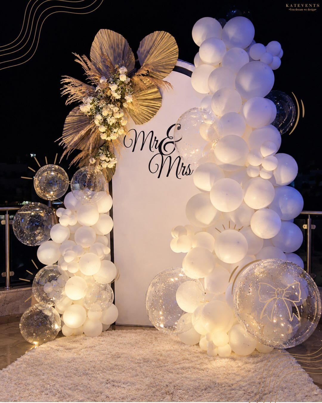 White wedding backdrop with balloon arches, dried palm leaves, and Mr & Mrs text.