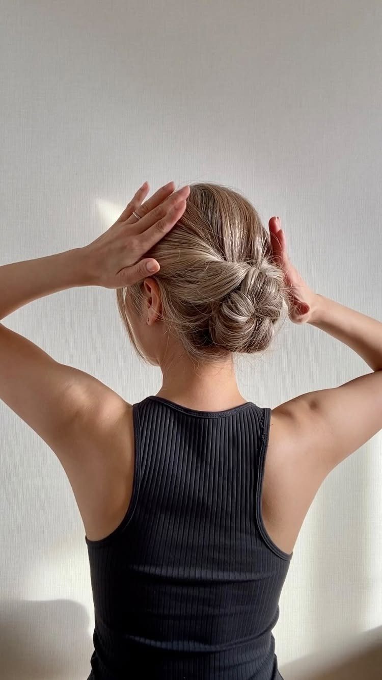 A woman with blonde hair styled in a braided low bun against a white wall.