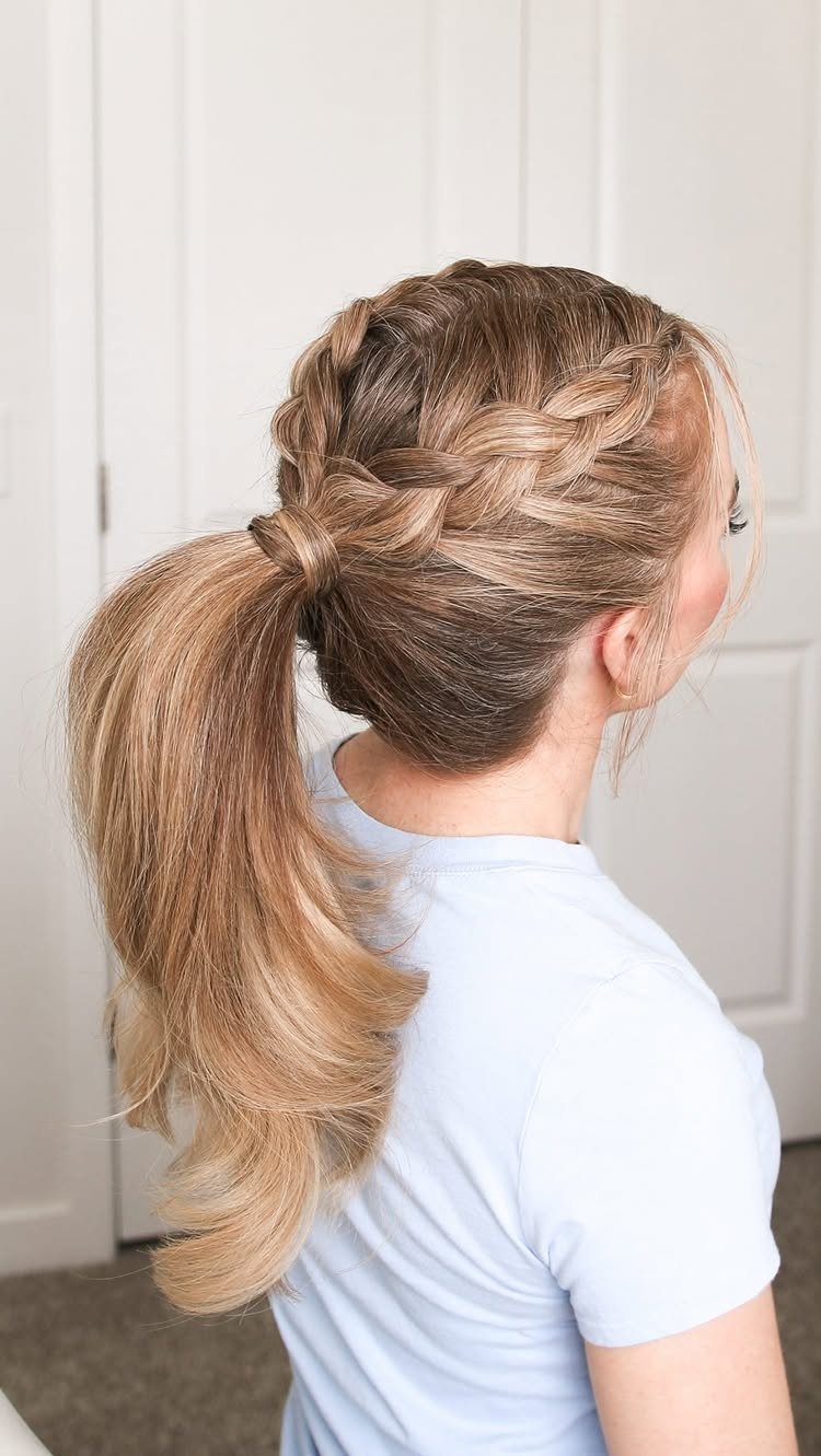 Blonde woman with a thick Dutch braid crown leading into a long wavy ponytail.