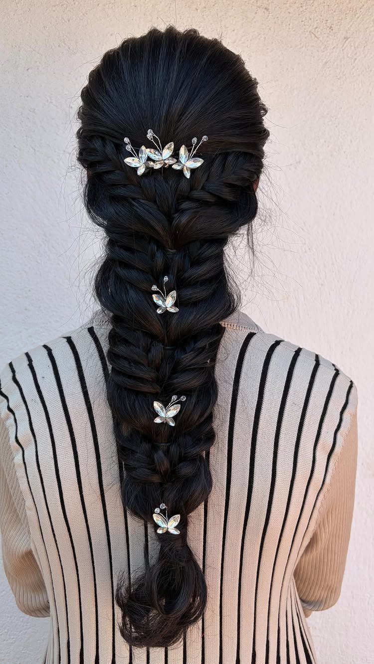 Long dark hair styled in a voluminous fishtail braid decorated with silver butterfly hair accessories.