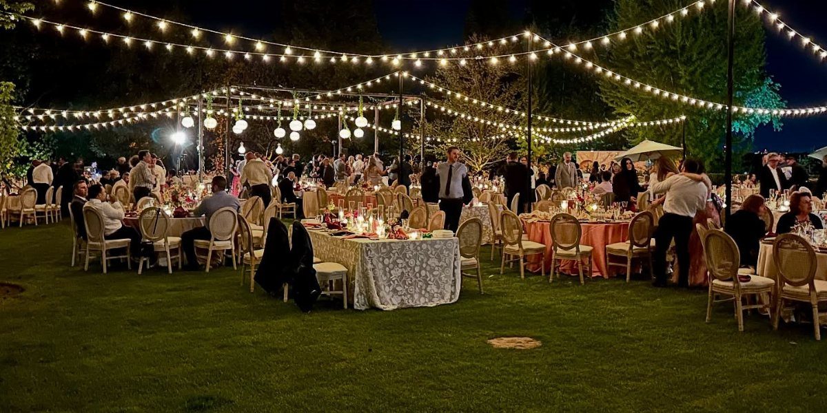 String lights hanging over guests seated at tables during an outdoor evening wedding reception.