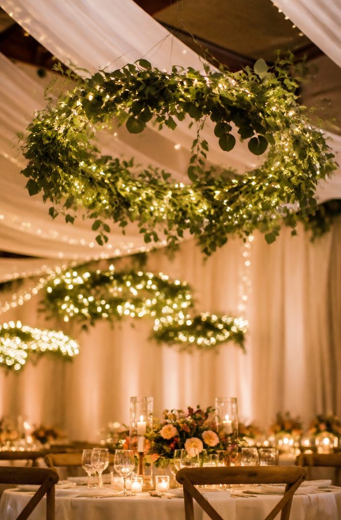 Suspended greenery hoops with fairy lights at a wedding venue.