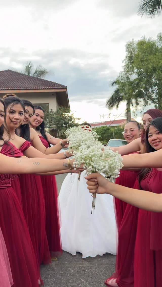 Bridesmaids in long red dresses holding white flower bouquets surrounding a bride in white.