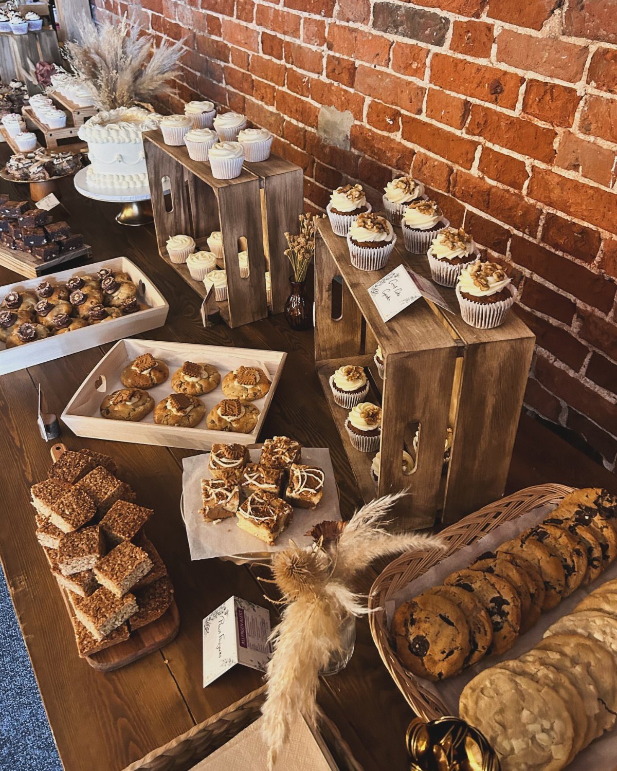 Various fall desserts like cupcakes, brownies, and cookies arranged on a wooden table against a brick wall.
