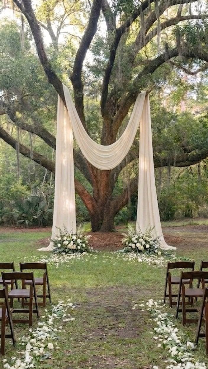 Cream fabric draped between large tree branches over a floral wedding ceremony setup.