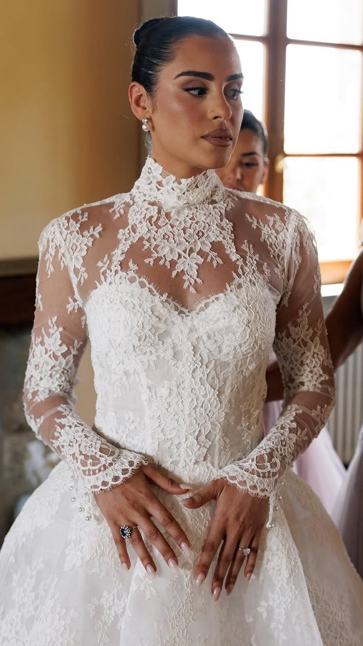 A woman wearing a white long-sleeved wedding dress with intricate lace detailing on the bodice and sleeves.