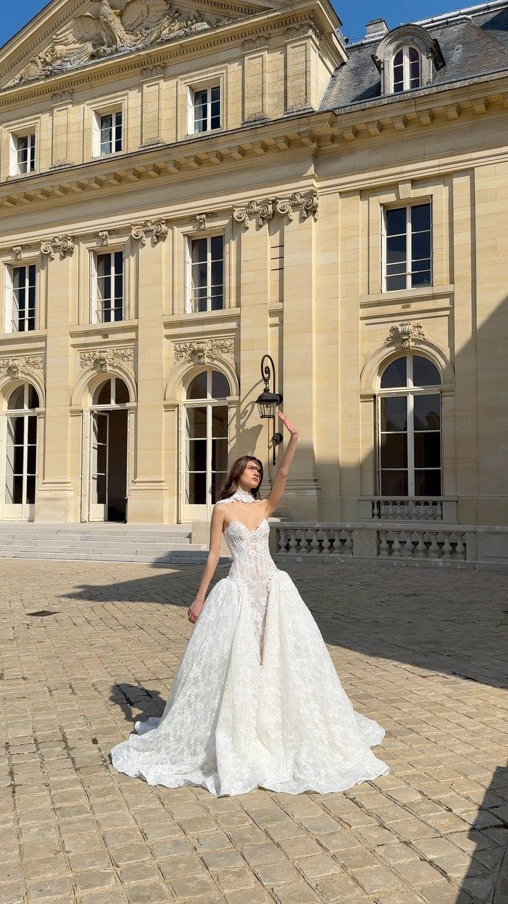 A woman wearing a fitted sculptural lace wedding dress standing in a sunny courtyard.