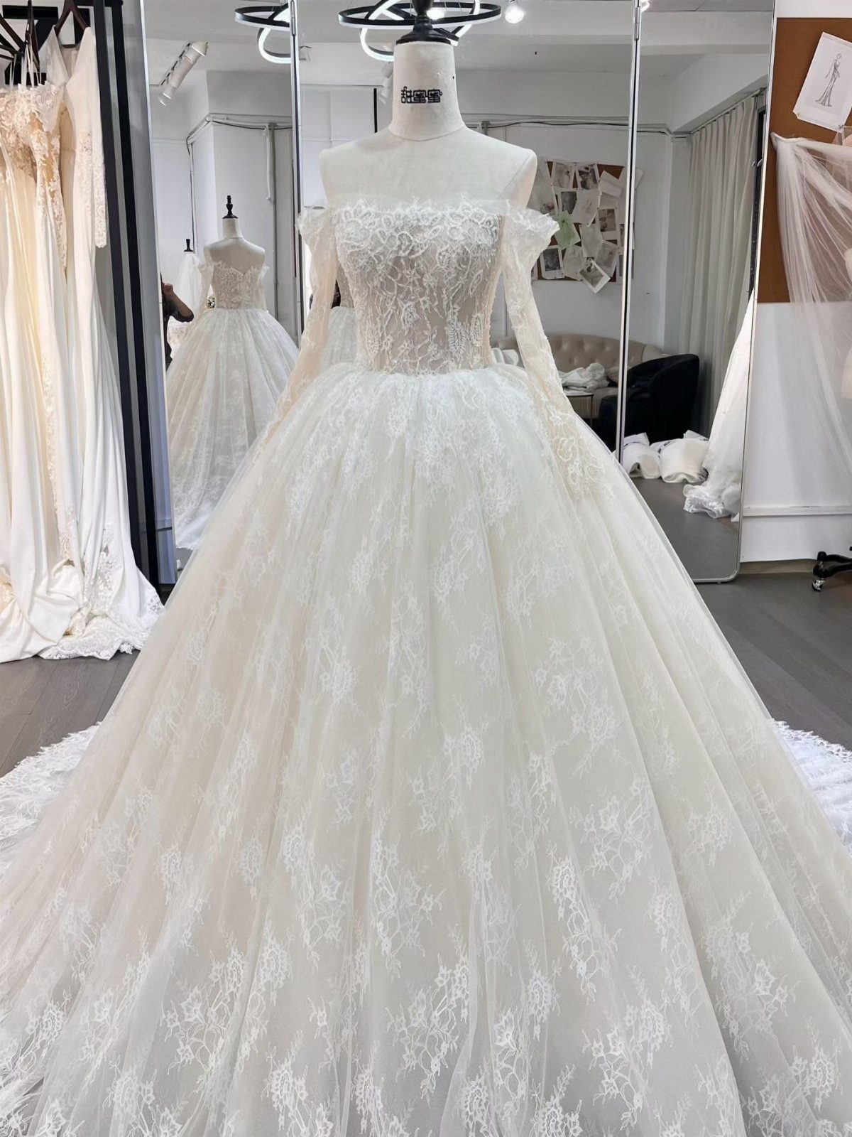 A white lace wedding dress with off-the-shoulder sleeves displayed on a mannequin.
