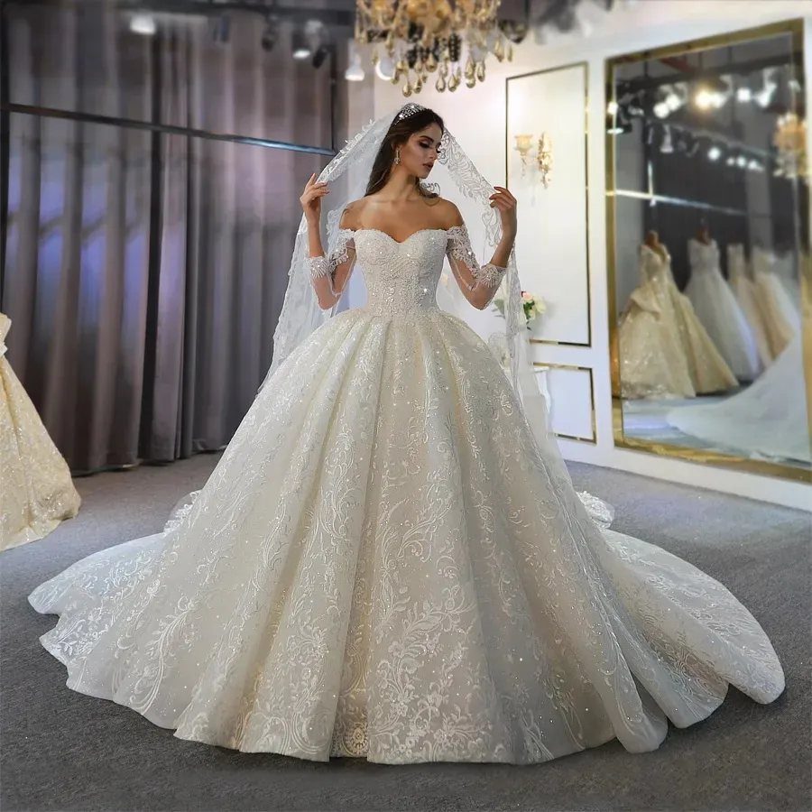 A woman posing in a voluminous white lace ball gown wedding dress with a long veil.