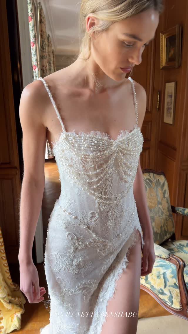 A blonde woman wearing an intricate, beaded vintage lace wedding dress with thin straps.