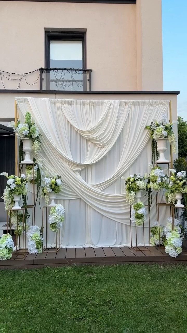 White fabric draped in elegant swags on a large wedding backdrop with floral arrangements.