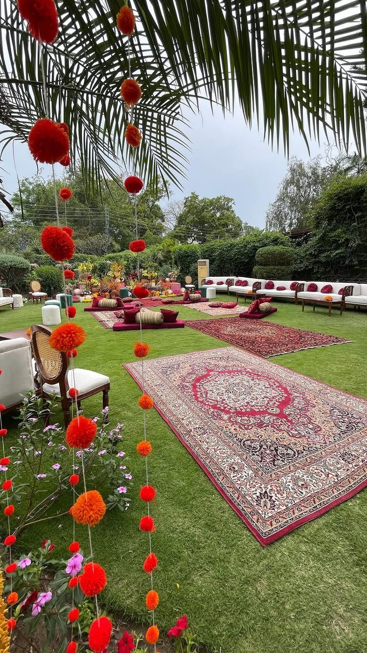 Red and orange pom-pom garlands hanging over a garden with rugs and white lounge seating.
