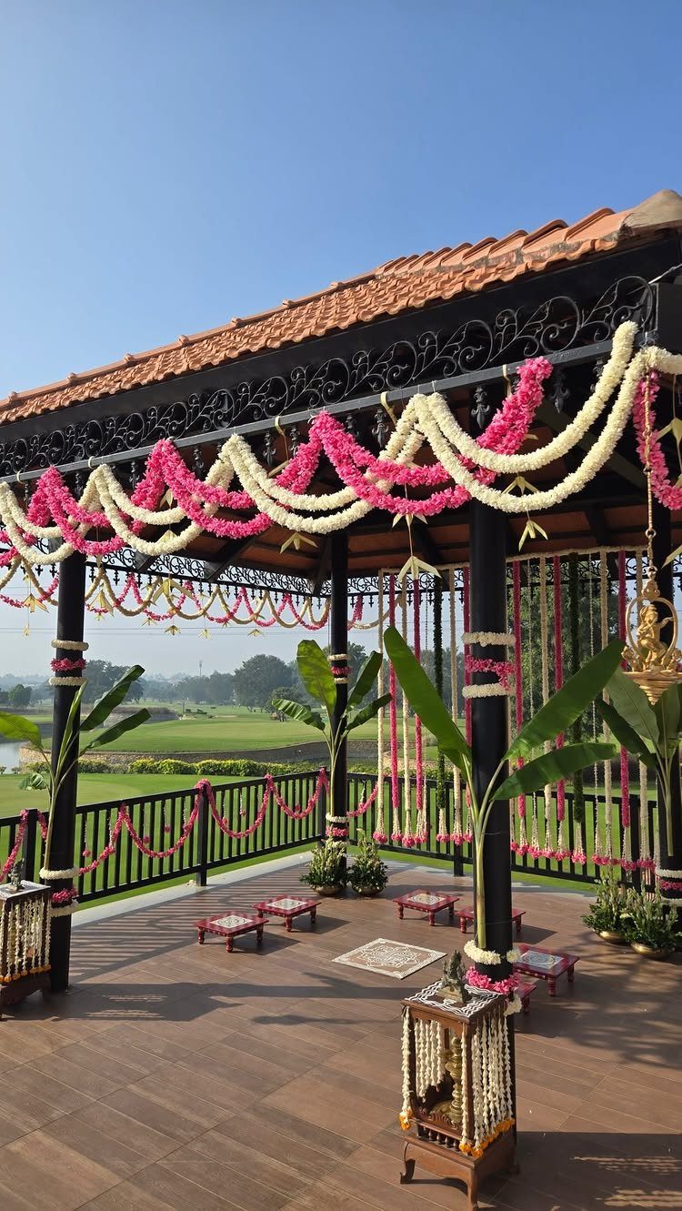 A decorated outdoor pavilion with pink and white flower garlands overlooking a green landscape.