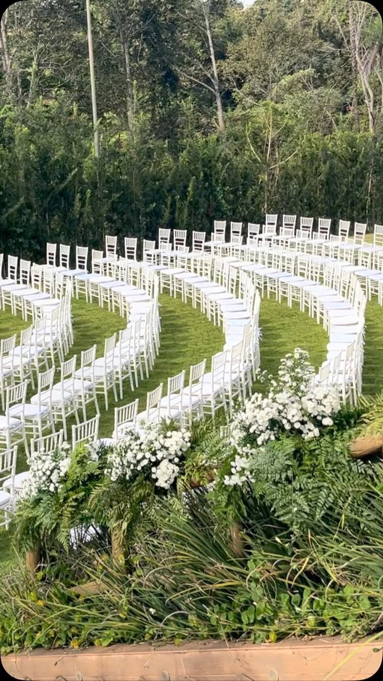 White chairs arranged in curved, concentric rows on a green lawn for an outdoor wedding ceremony.